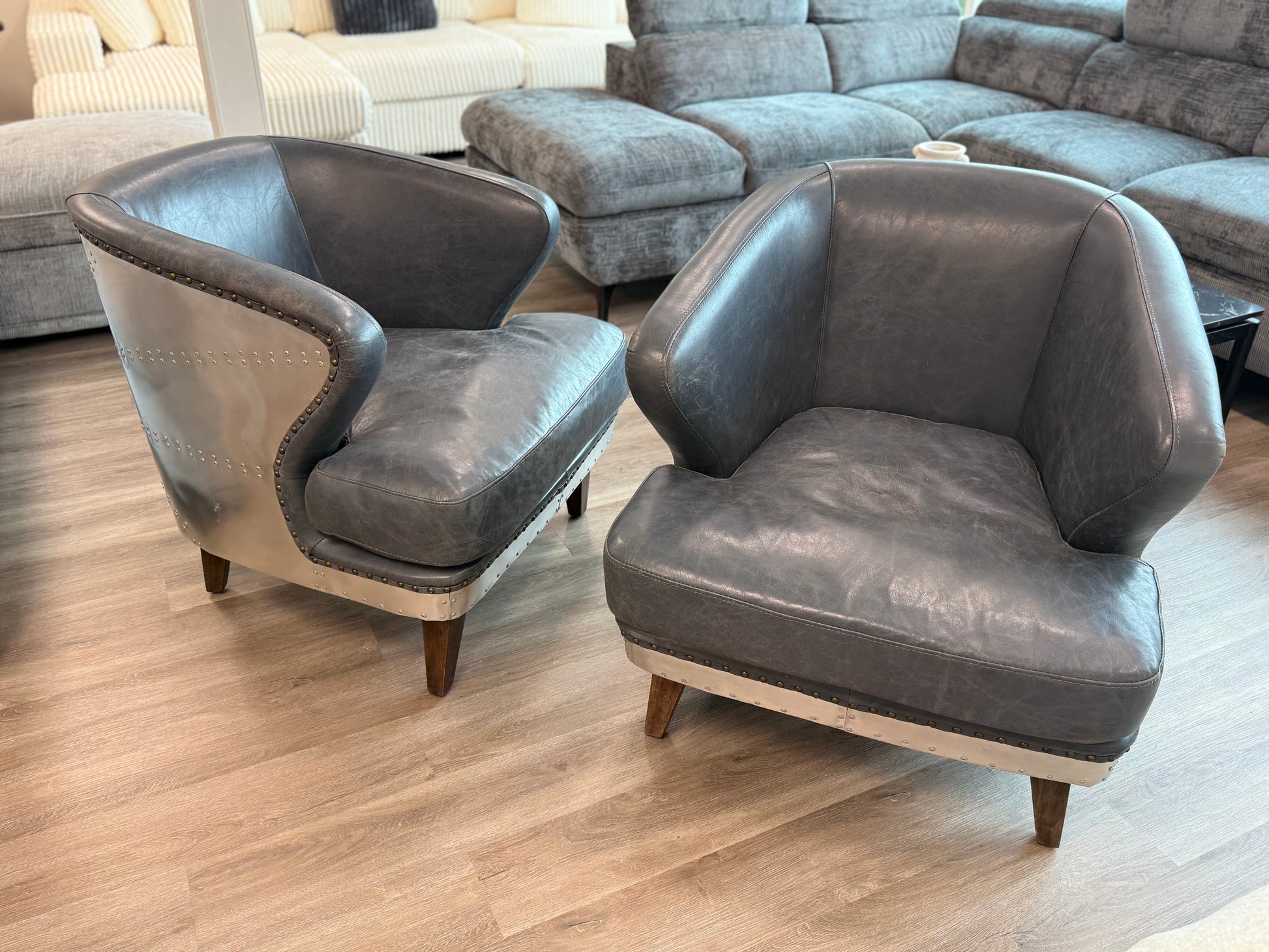 Two gray armchairs in a living room setting with a couch in the background.