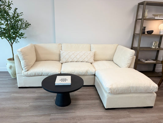 White sectional sofa in a living room with a black coffee table and plant.