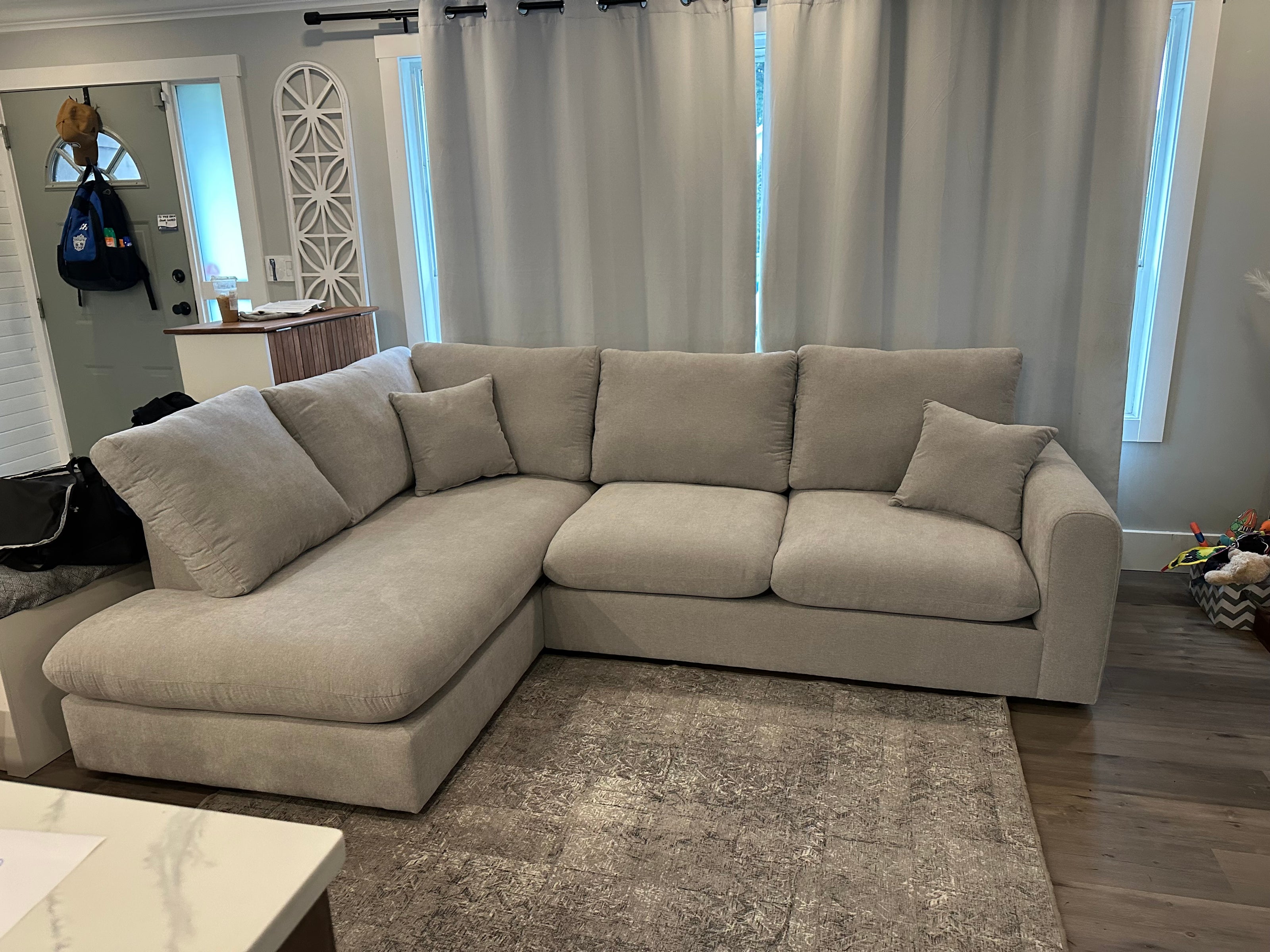 Gray sectional sofa in a living room with curtains and a mirror.