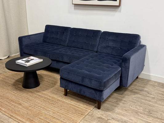 Navy blue sectional sofa in a living room setting with a small round table.