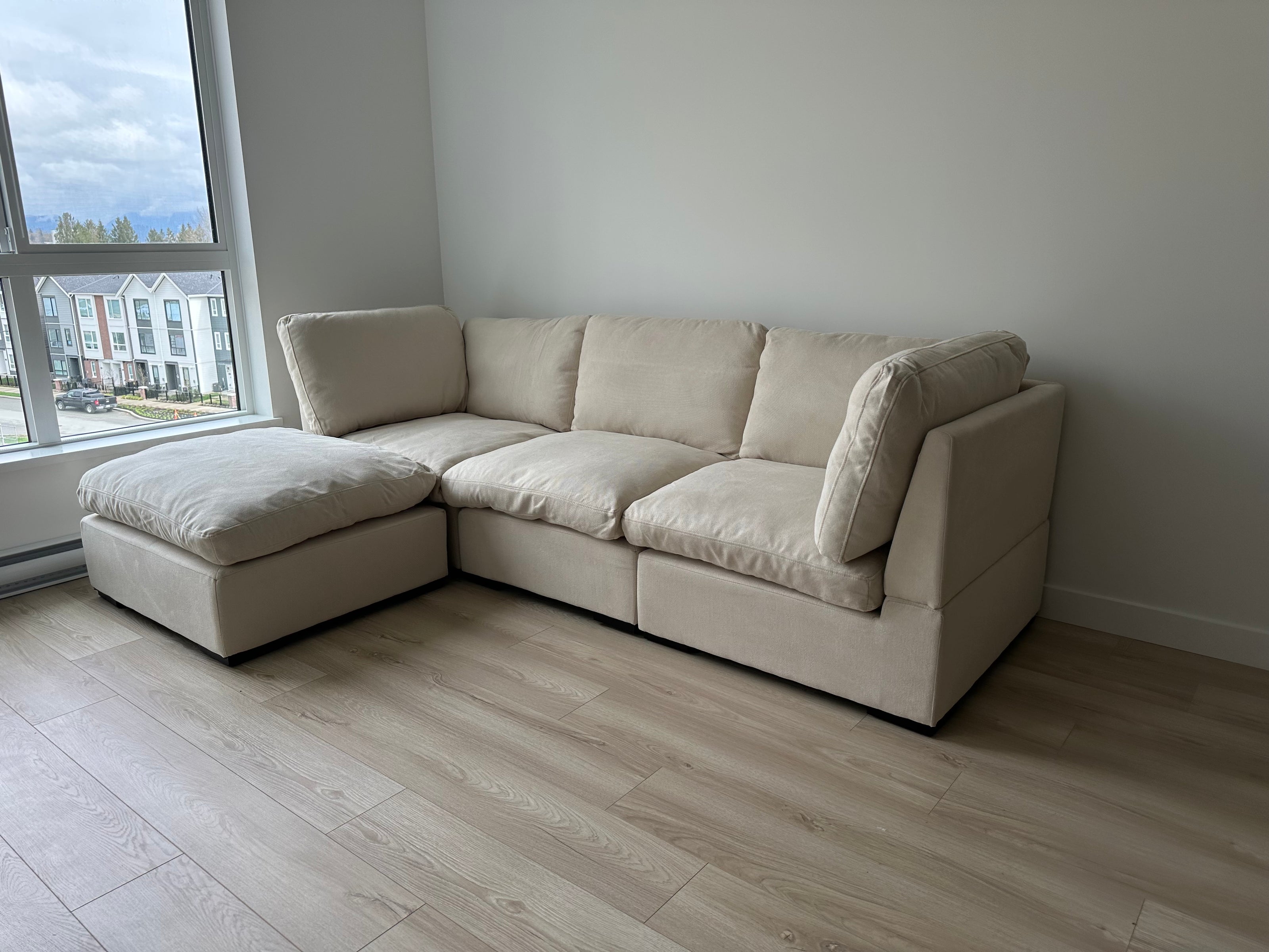 Beige cloud couch sectional sofa in a room with large windows.