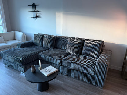 Gray Soft corduroy sectional sofa in a living room with a small round table and decor items.