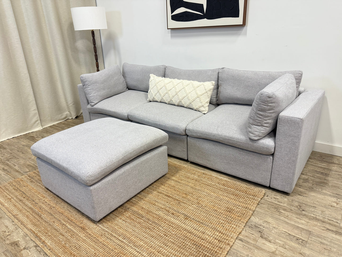 Gray sectional sofa with ottoman on a wooden floor in a living room setting.