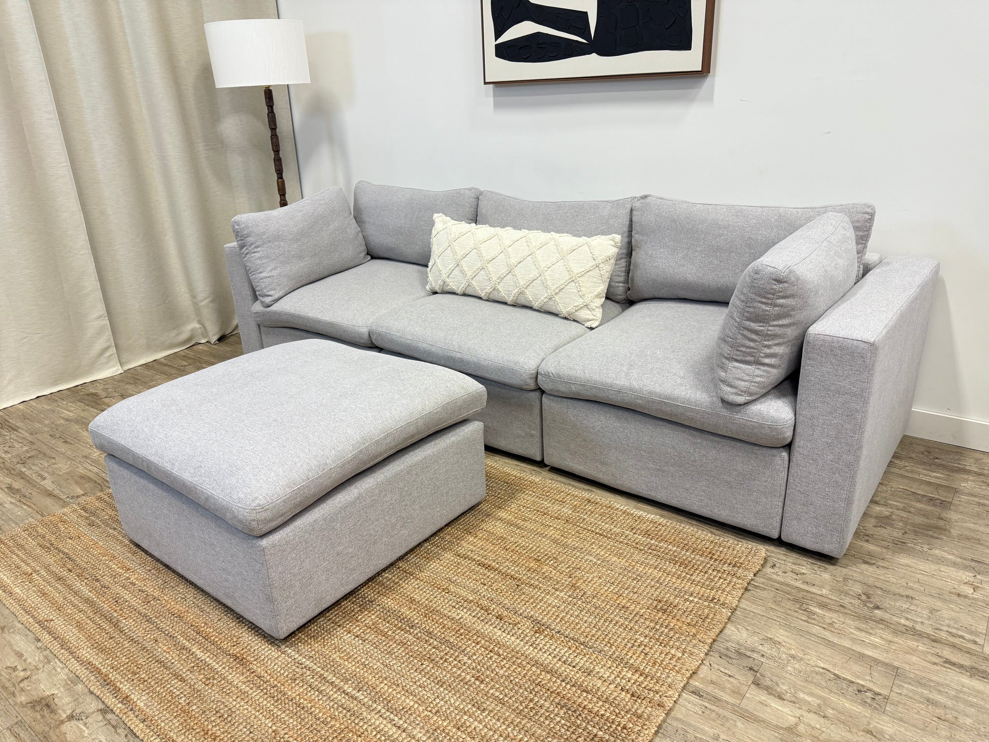 Gray sectional sofa with ottoman on a wooden floor in a living room setting.